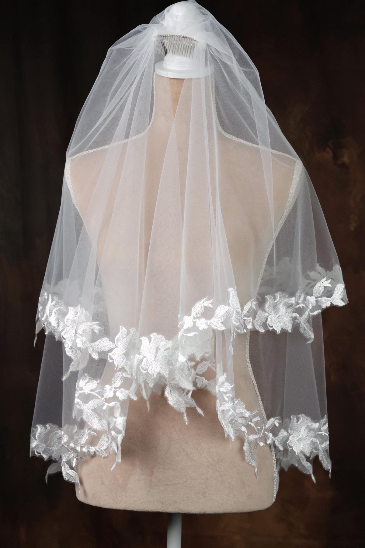 A white wedding veil with delicate lace trim is displayed on a mannequin.