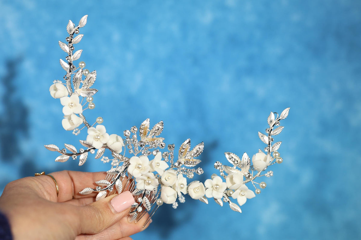 A hand holding a decorative piece of white floral jewelry against a blue background.