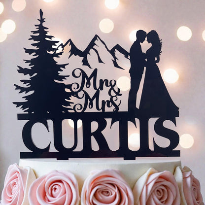 A silhouette of a couple embracing, with mountains in the background, and the name "CURTIS" written on a cake topper.