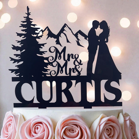 A silhouette of a couple embracing, with mountains in the background, and the name "CURTIS" written on a cake topper.