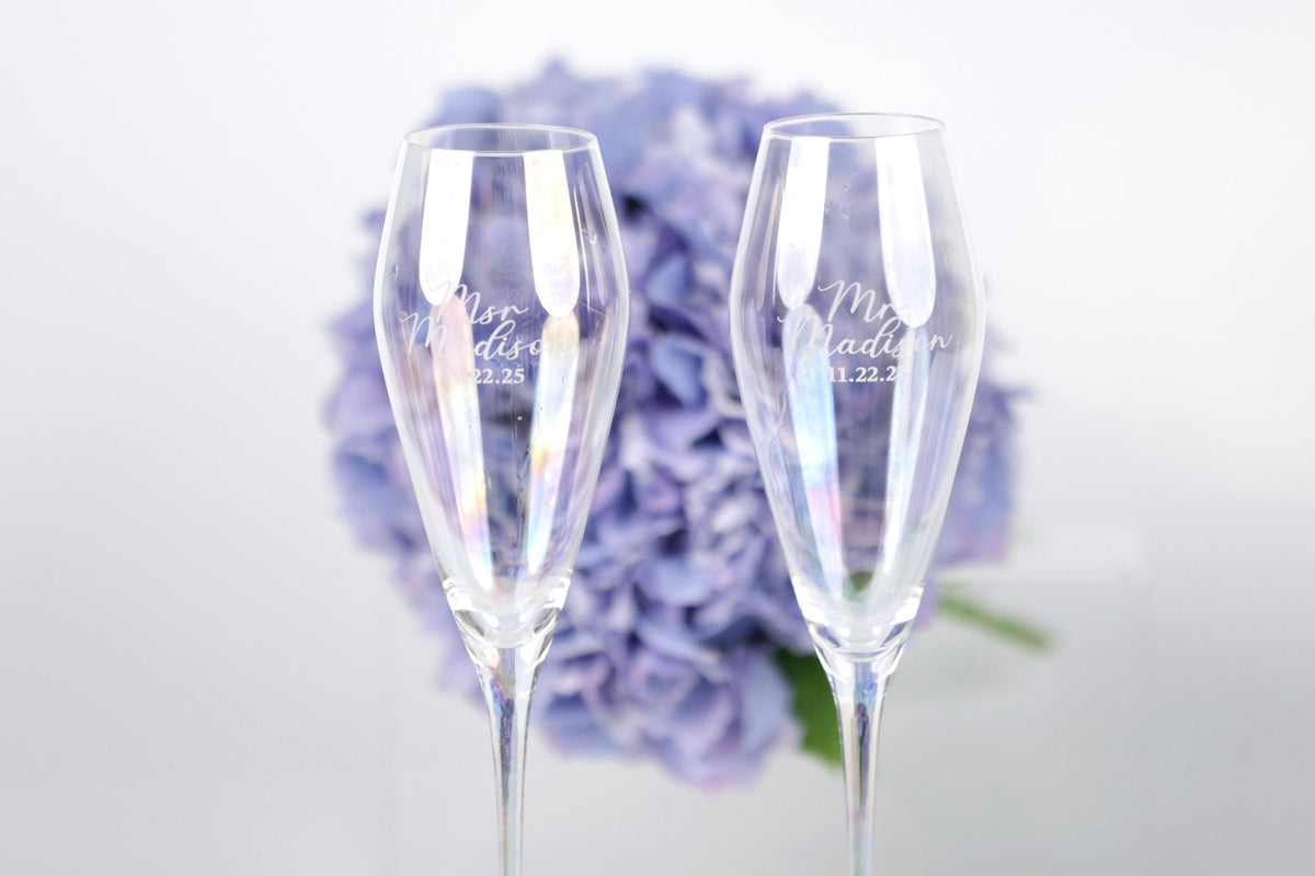 two champagne flutes with personalized messages, placed in front of a background of purple flowers.