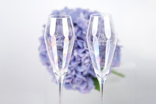 two champagne flutes with personalized messages, placed in front of a background of purple flowers.