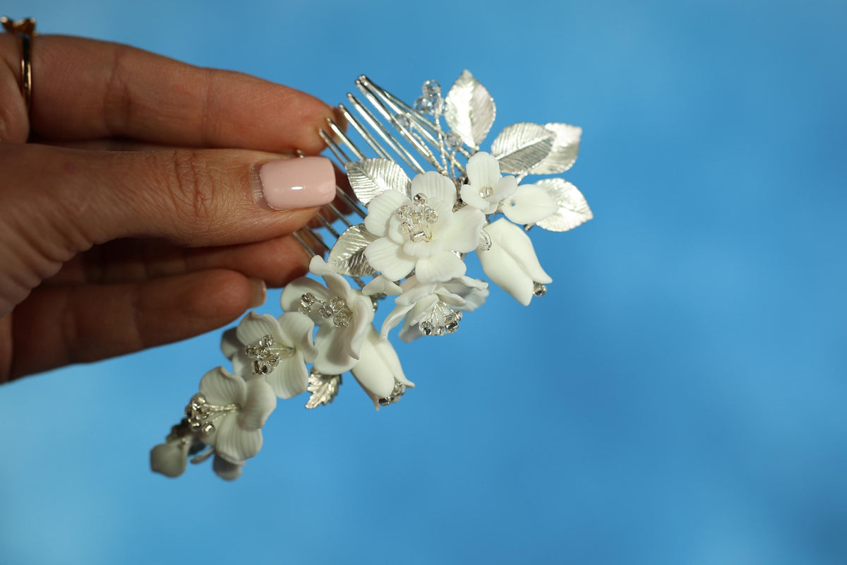 A hand holding a silver hairbrush adorned with white flowers against a blue background.