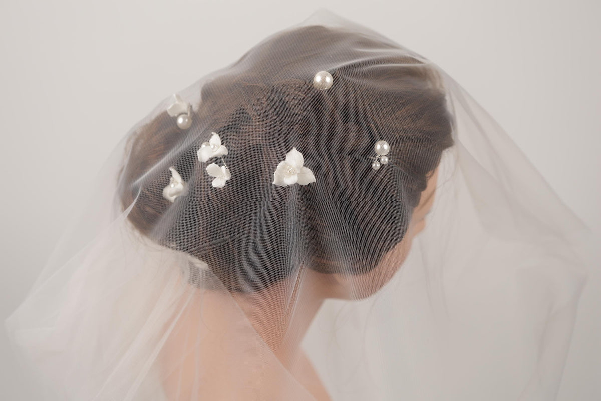 A woman's head is partially obscured by a veil, with her hair styled in an updo and adorned with small white flowers.