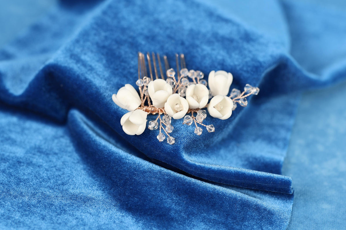 A close-up view of a decorative hair clip with white flowers and clear gemstones, resting on a blue velvet background.