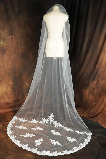 A white wedding veil with a lace trim is displayed on a mannequin against a brown background.