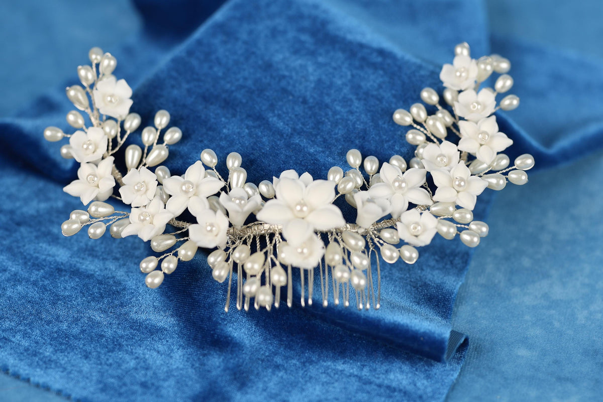 A decorative hair accessory with white flowers and pearls is displayed on a blue velvet background.