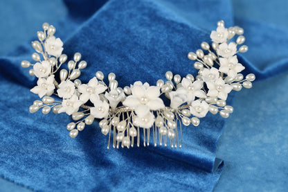 A decorative hair accessory with white flowers and pearls is displayed on a blue velvet background.