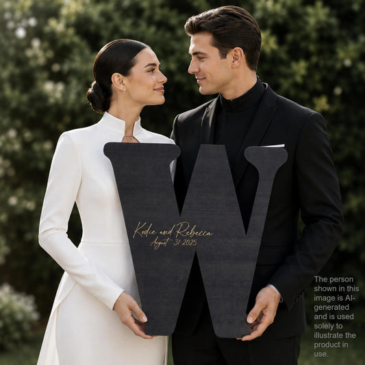 A man and a woman standing together, holding a large black letter 'W' with the text "Kobe and Rebecca August 25, 2015" written on it.