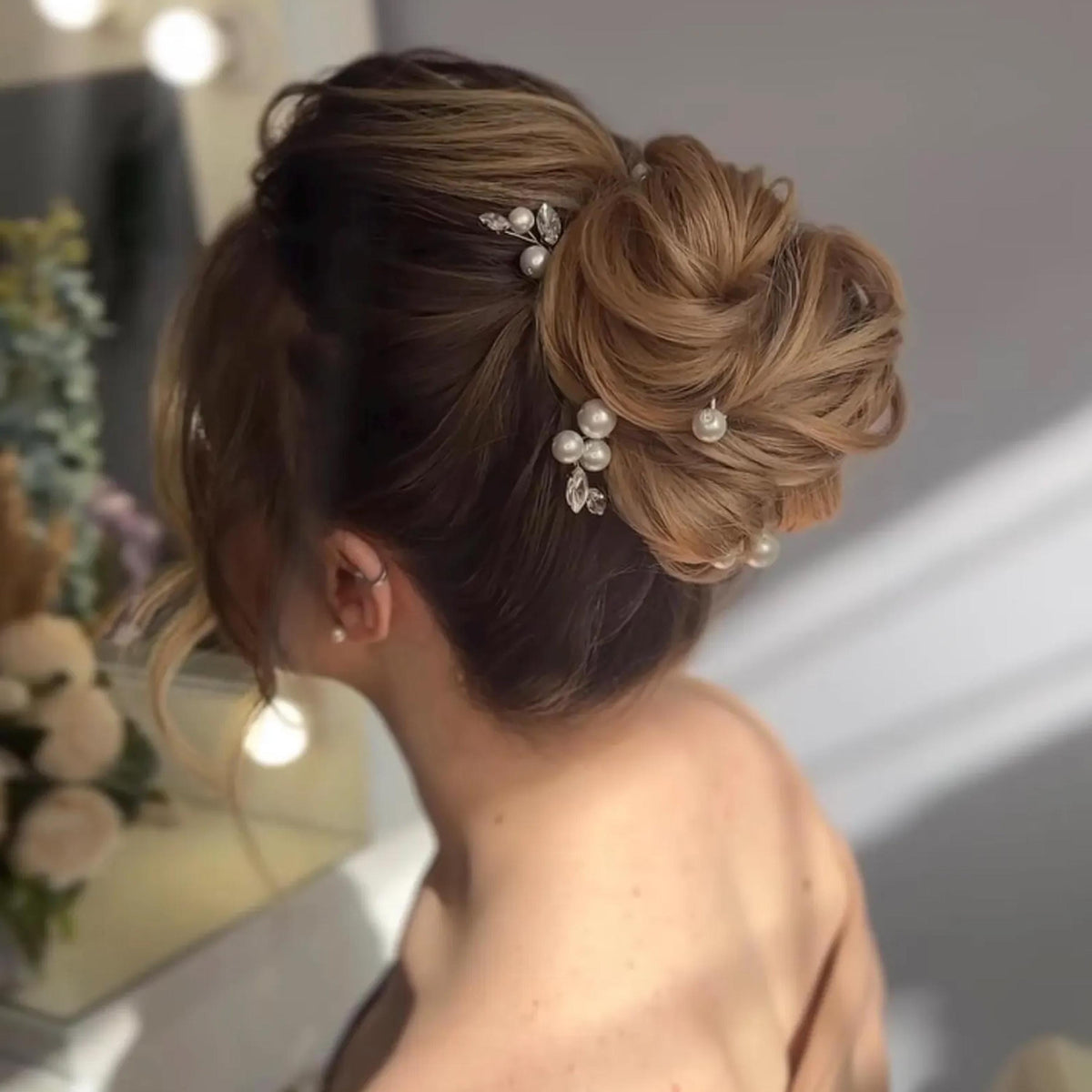 A woman with her hair styled in an updo, adorned with pearl hair clips.
