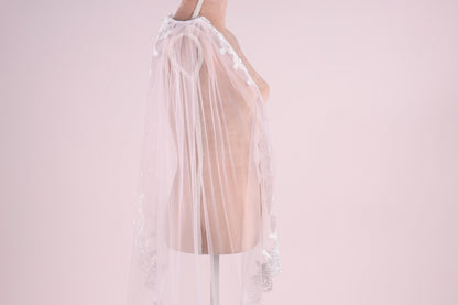 A mannequin wearing a white lace veil with a delicate floral pattern.