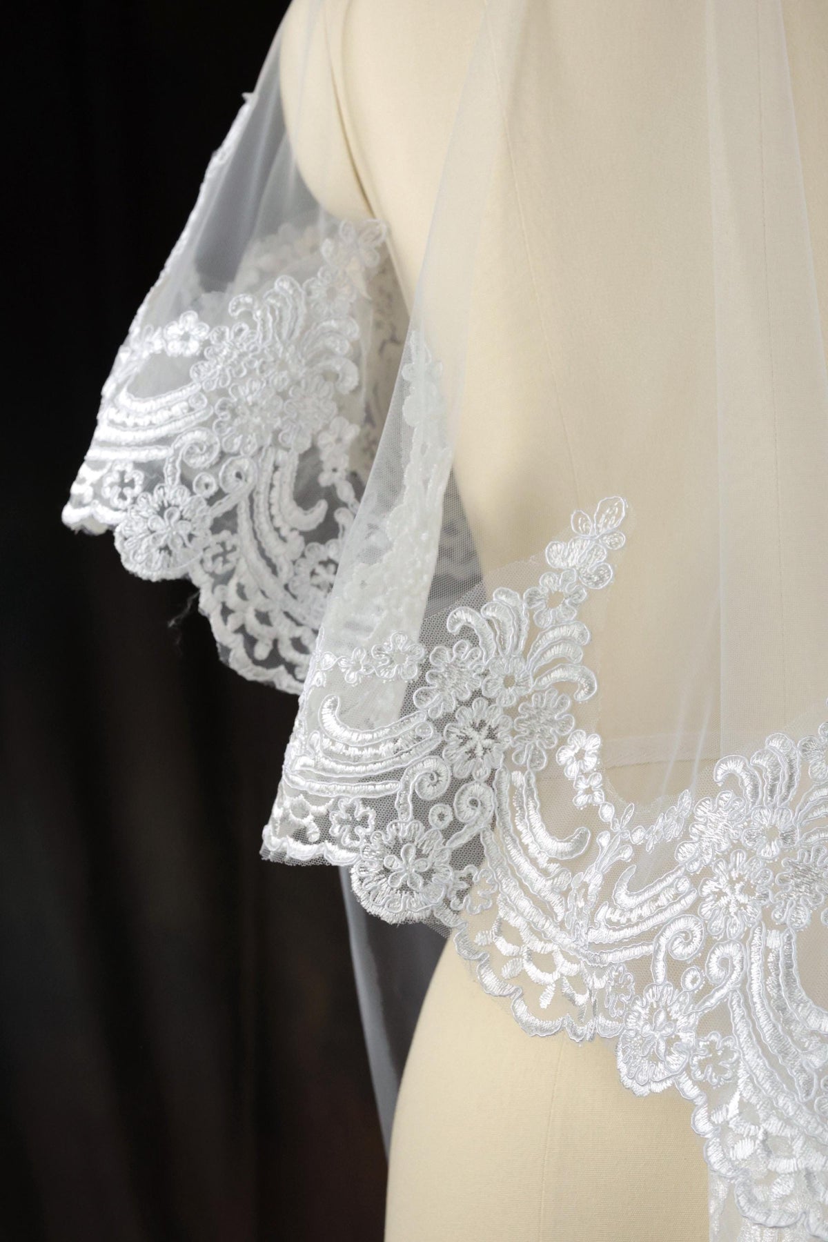 A close-up view of a delicate white lace veil with intricate floral embroidery, displayed on a mannequin.