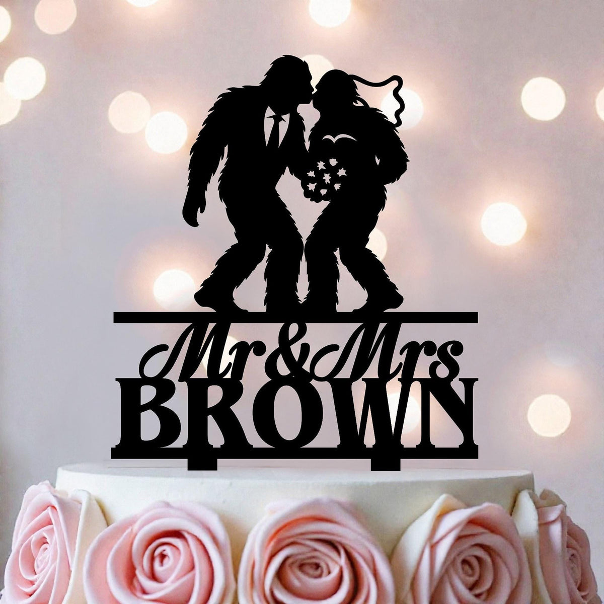 A black silhouette of a man and a woman kissing on top of a white cake, with the text "Mr & Mrs BROWN" below the silhouette.
