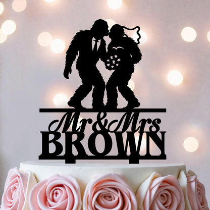 A black silhouette of a man and a woman kissing on top of a white cake, with the text "Mr & Mrs BROWN" below the silhouette.