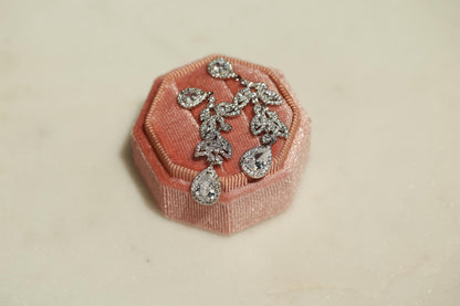 A pair of elegant diamond earrings rests on a pink velvet box, showcasing their intricate design and sparkling gemstones.
