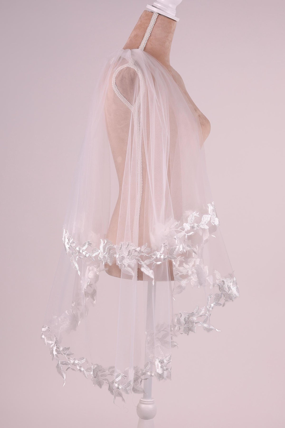 A mannequin wearing a white veil with delicate floral embroidery.