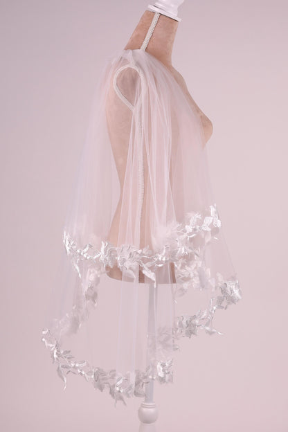 A mannequin wearing a white veil with delicate floral embroidery.