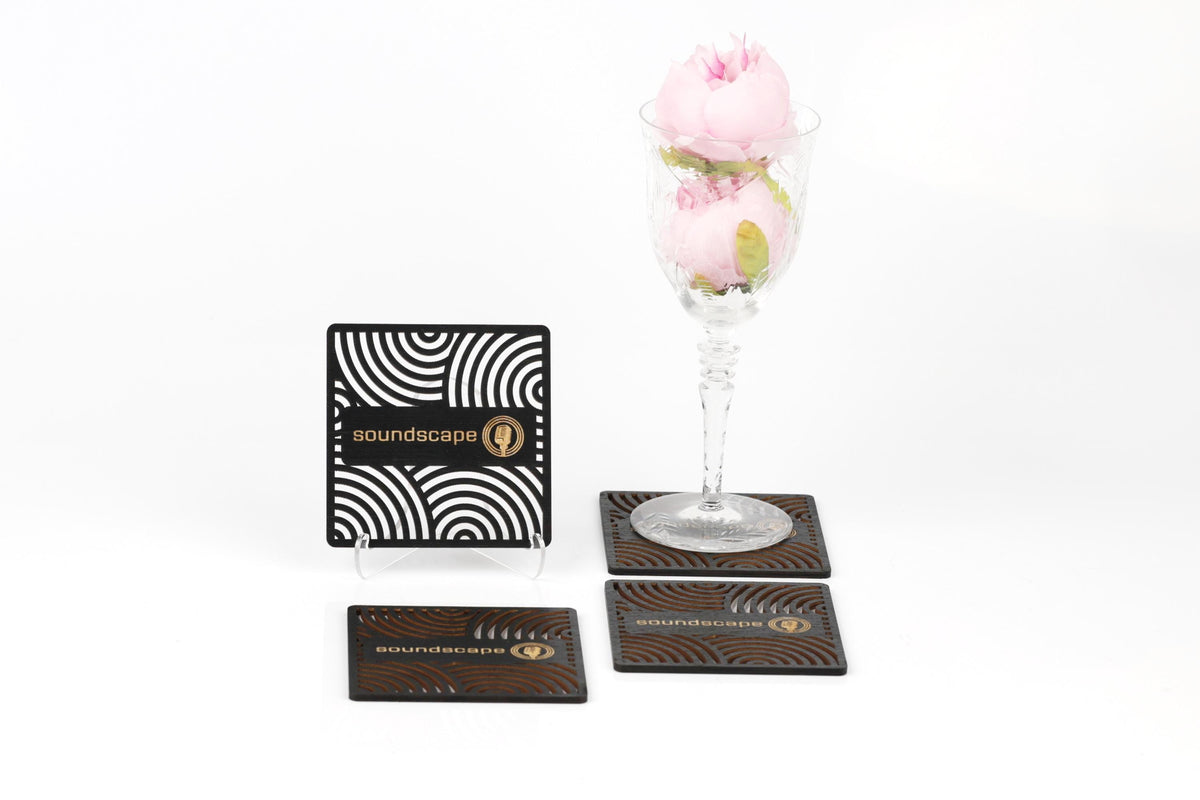 a glass vase with pink roses, a black and white coaster with the word "soundscape" written on it, and two coasters with the same design.