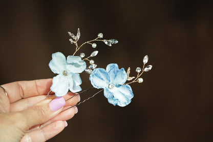 A hand holding a pair of delicate flower-shaped hair clips adorned with sparkling rhinestones.