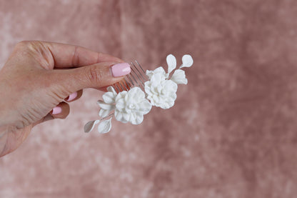 A hand holding a white flower-shaped hair accessory against a pink background.