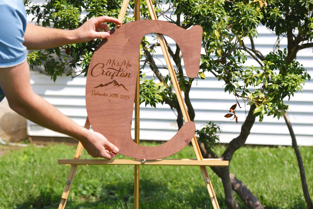 A person is holding a wooden sign with the name "Mrs. Crafton" and the date "September 29, 2015" on it, standing in front of a tree.