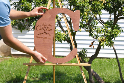 A person is holding a wooden sign with the name "Mrs. Crafton" and the date "September 29, 2015" on it, standing in front of a tree.