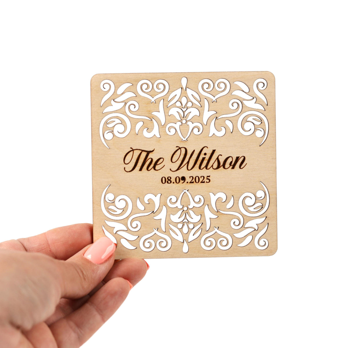 A hand holding a wooden card with a decorative floral design and text on it.