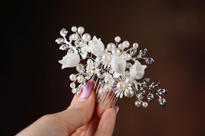 A hand holding a decorative hair clip with white flowers and pearls.