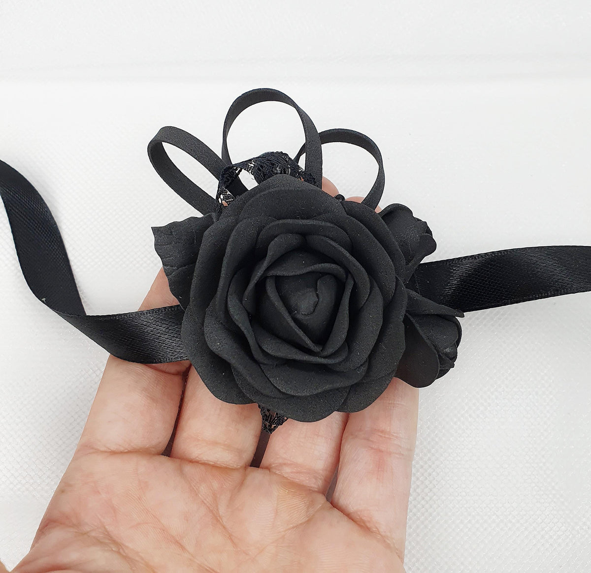 a hand holding a black rose on a black ribbon