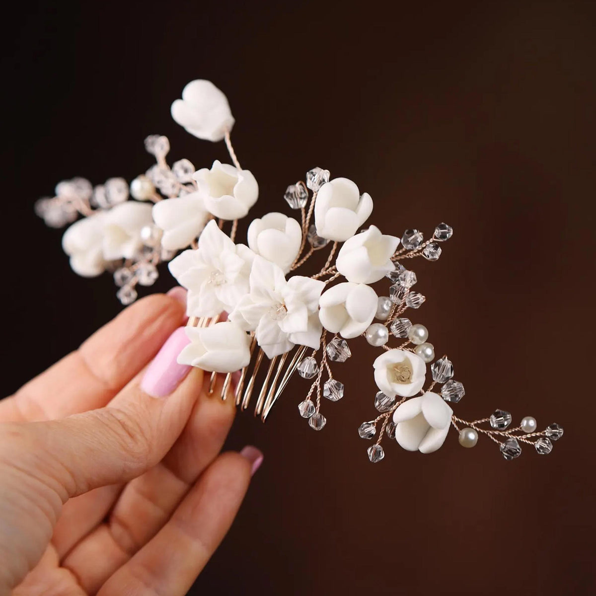 A hand holding a decorative hair clip with white flowers and clear gemstones.