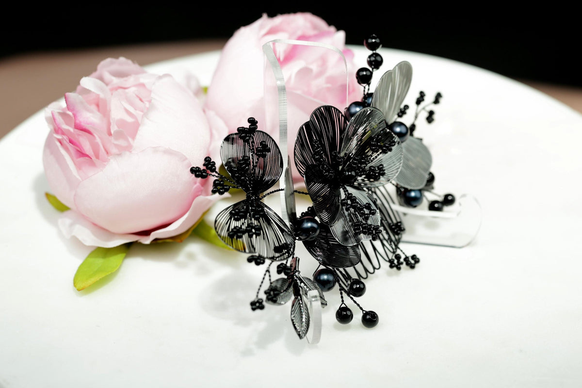 A close-up view of a decorative hair accessory with black and silver elements, including a butterfly-shaped element, placed on a white surface.