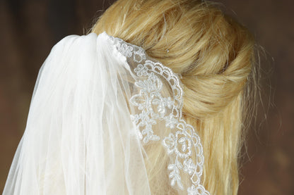 A close-up view of a woman's blonde hair styled in a twisted updo, with a white lace veil draped over her head.
