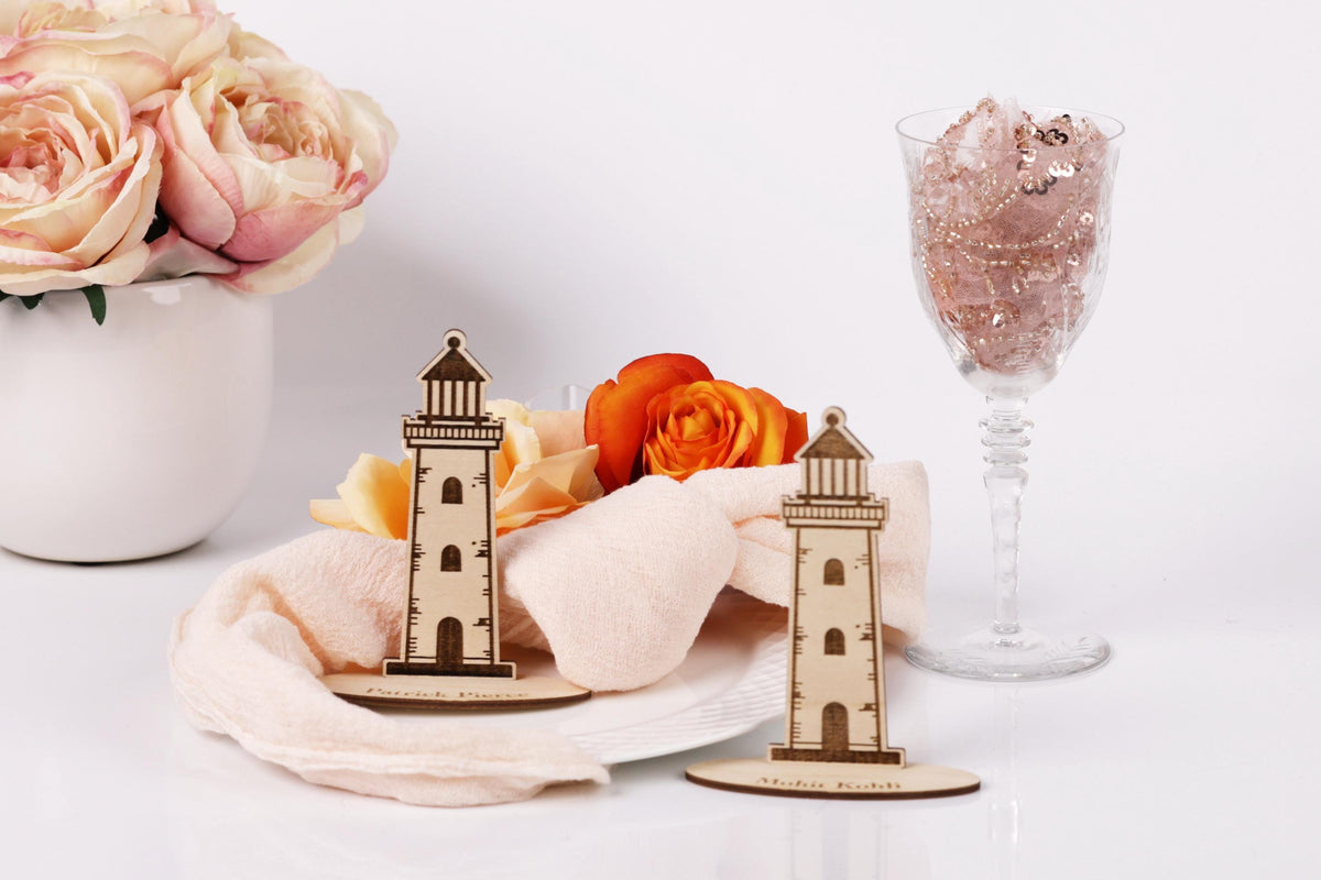 a table setting with a vase of pink roses, a glass of wine, and two wooden lighthouse-shaped place cards.