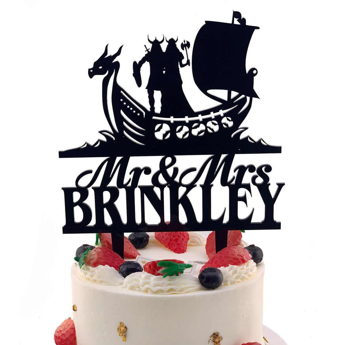A black silhouette of a couple on a boat with a dragon, along with the text "Mr & Mrs BRINKLEY" on a cake topper.