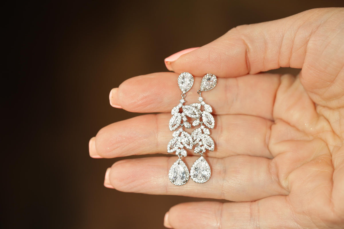A hand holding a pair of diamond earrings with intricate floral designs.