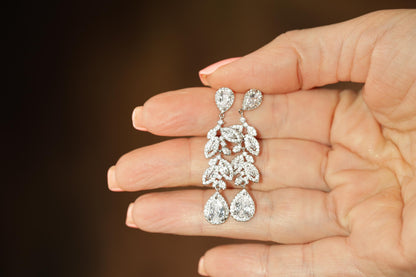 A hand holding a pair of diamond earrings with intricate floral designs.
