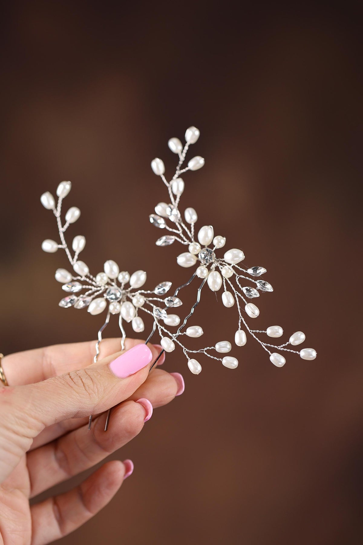 A hand holding a decorative hair accessory with white flowers and pearls.