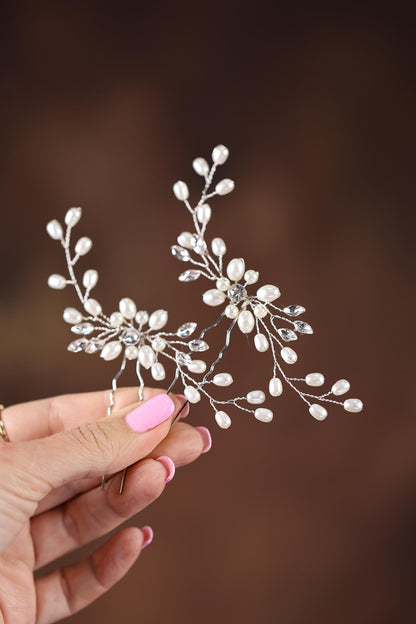 A hand holding a decorative hair accessory with white flowers and pearls.