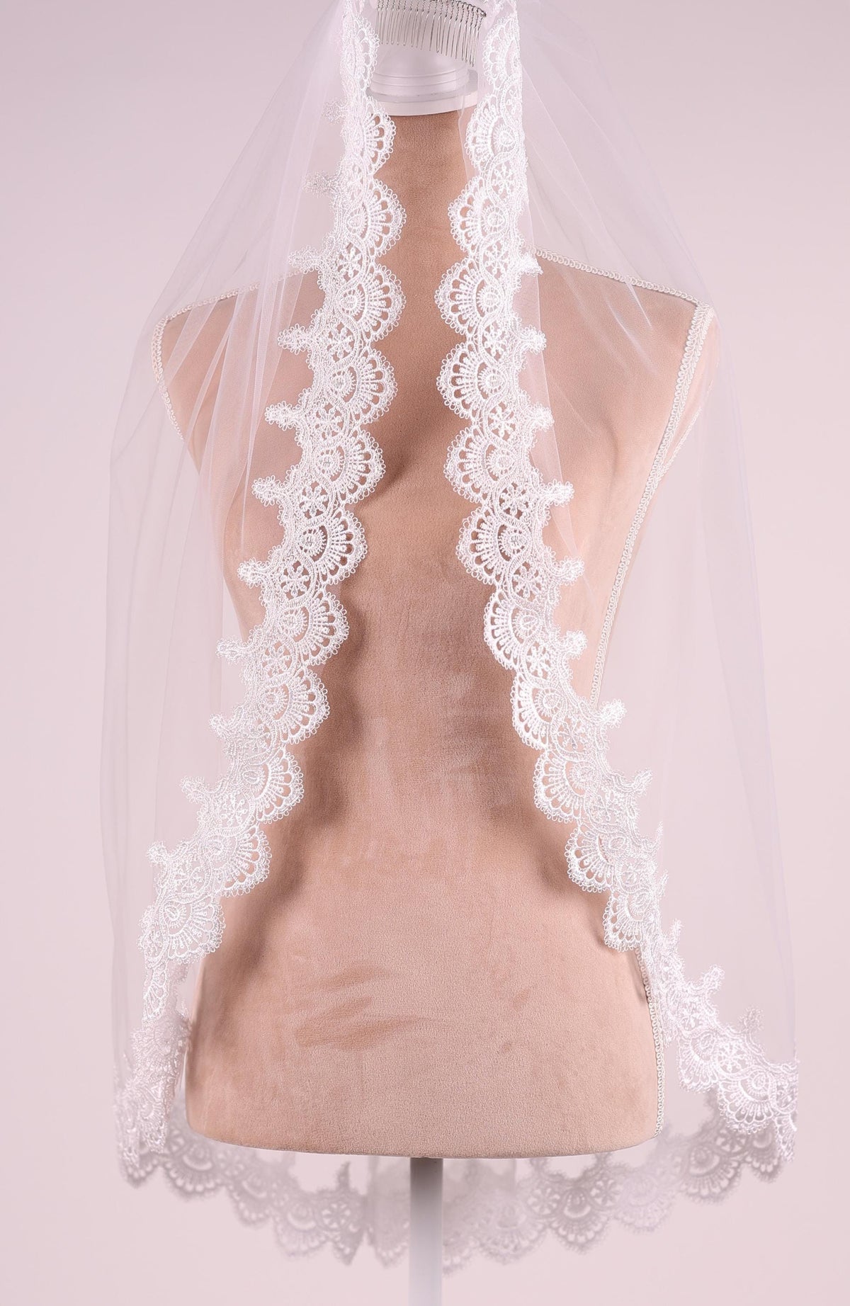 A mannequin wearing a white lace veil with a scalloped edge.