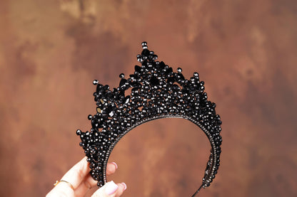 a hand holding a black tiara against a brown background