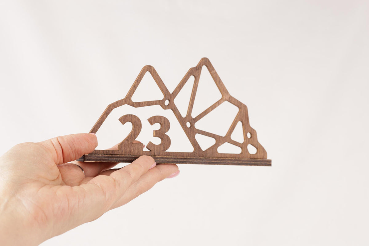 A hand is holding a wooden object that appears to be a mountain-shaped design with the number 23 on it.