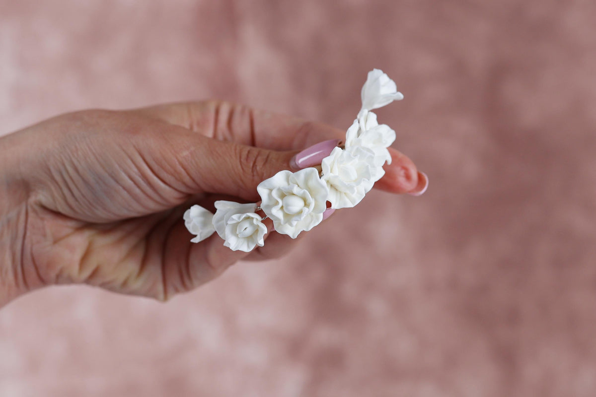A hand holding a delicate arrangement of white flowers against a pink background.