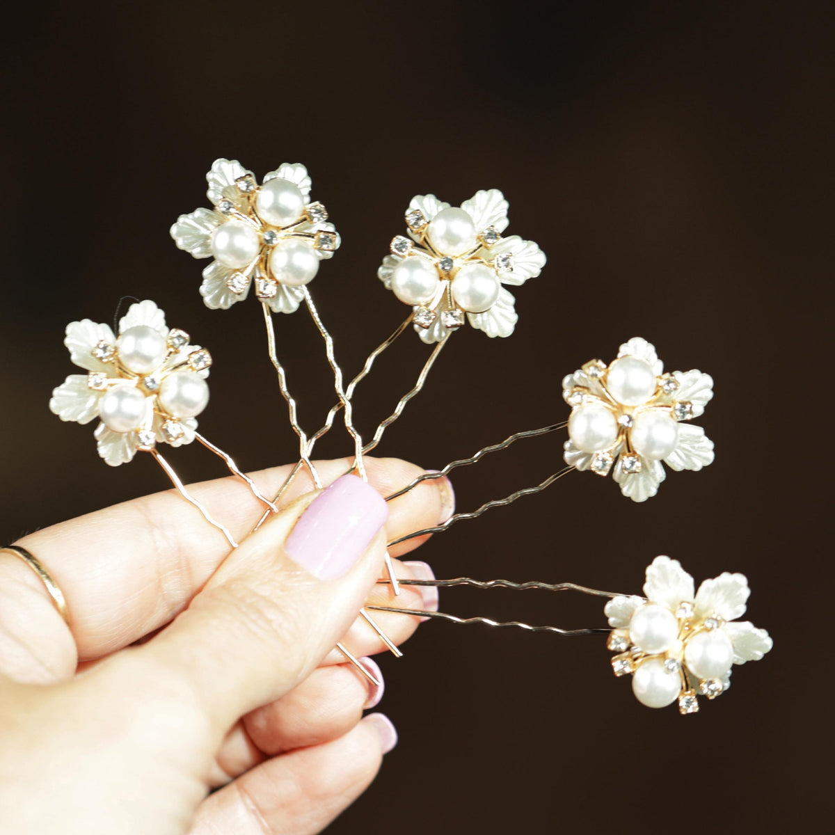 A hand holding a group of ornate hair clips with white flowers and rhinestones.