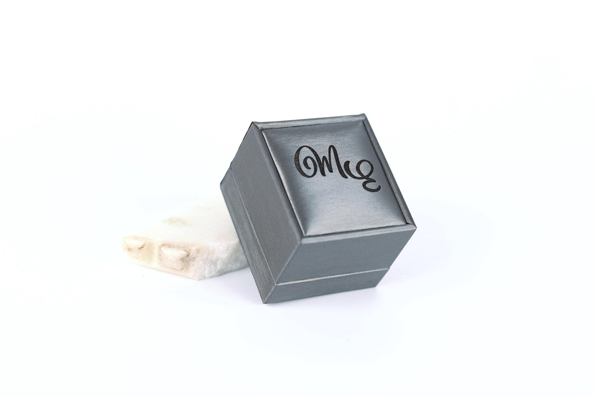 A gray metal box with the word "Omig" written on it, placed on a white surface.