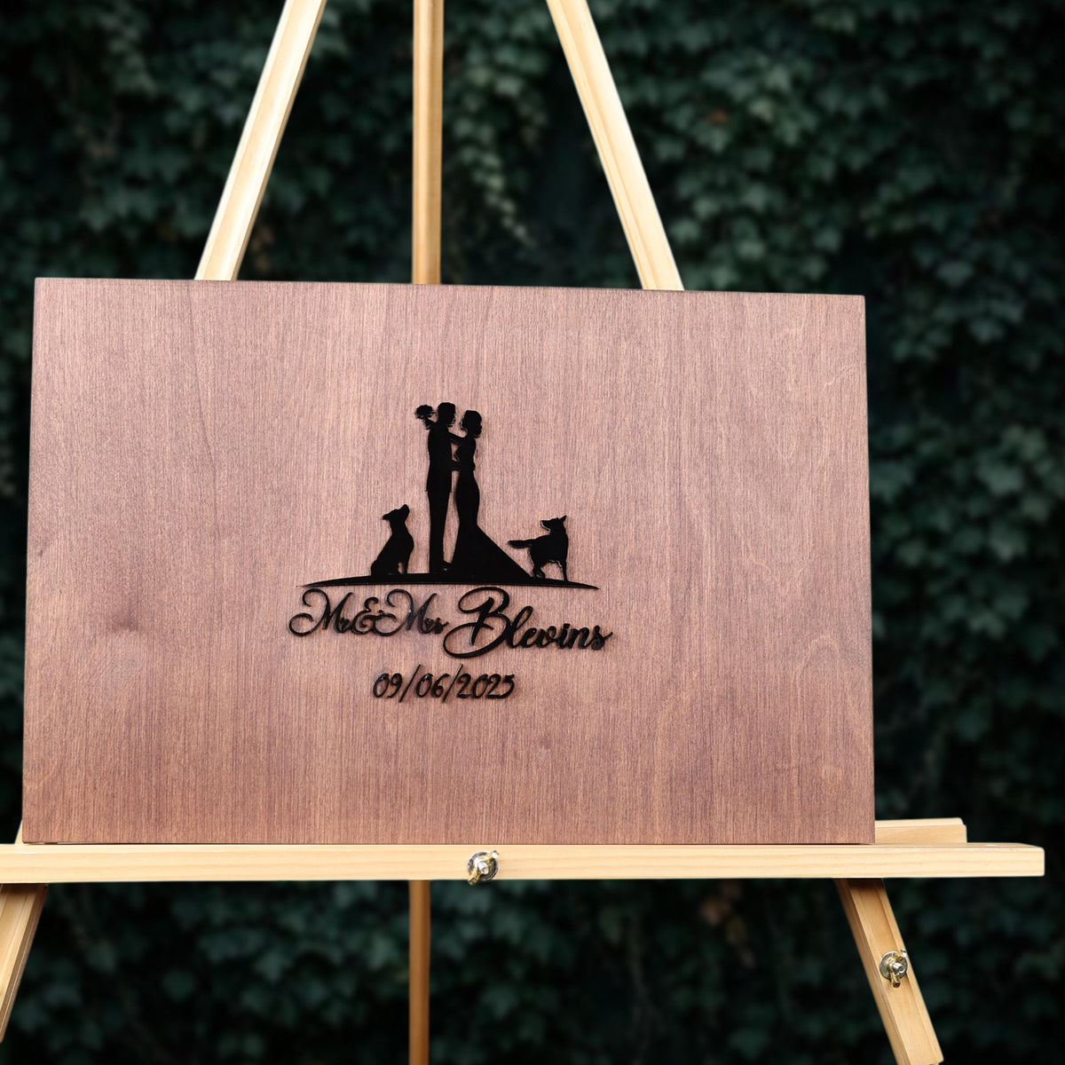 A wooden plaque with a silhouette of a couple and a dog, along with the text "Mr & Mrs Bloins 09/06/2022" on it.