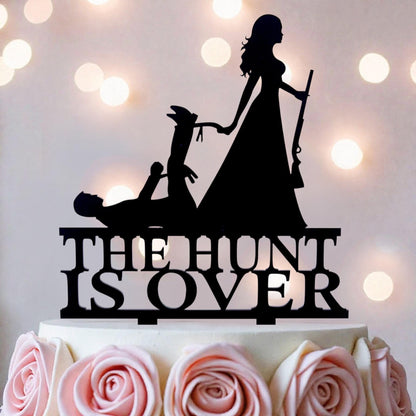 a cake with a black silhouette of a woman holding a gun, standing on top of it, and the words "THE HUNT IS OVER" written on the cake.