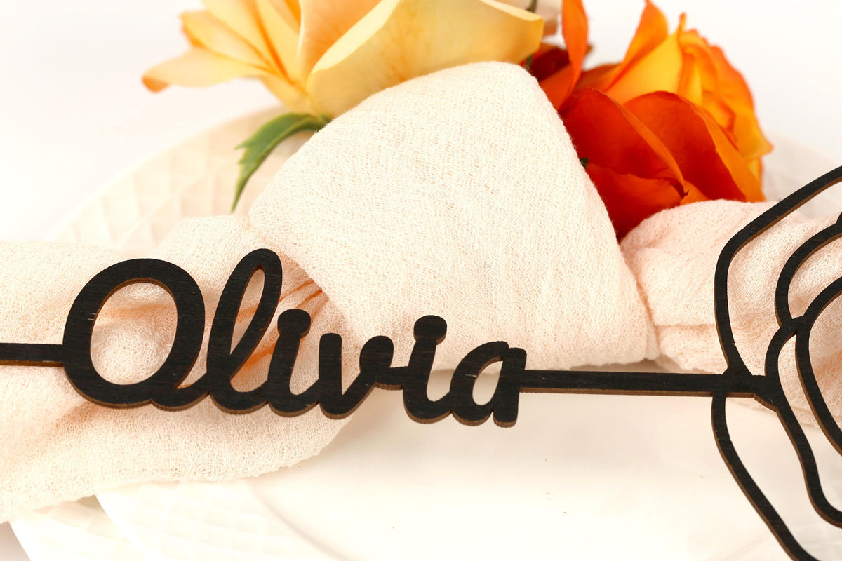 A close-up image of a decorative nameplate with the name "Olivia" written on it, surrounded by a floral arrangement of yellow and orange roses.