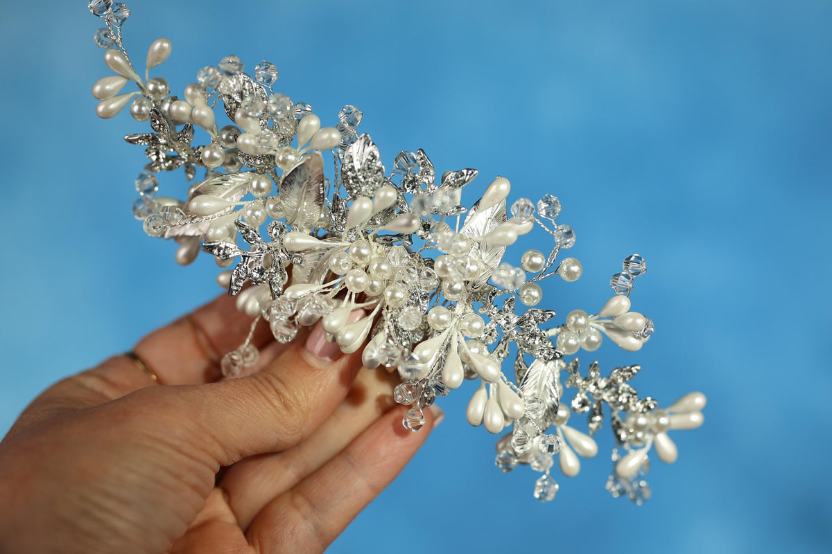A hand holding a decorative piece of jewelry, which appears to be a bracelet or headpiece, against a blue background.