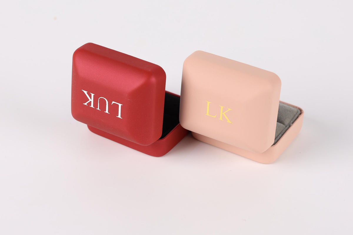 Two metal jewelry boxes, one red and one pink, with the letters "LK" printed on them.