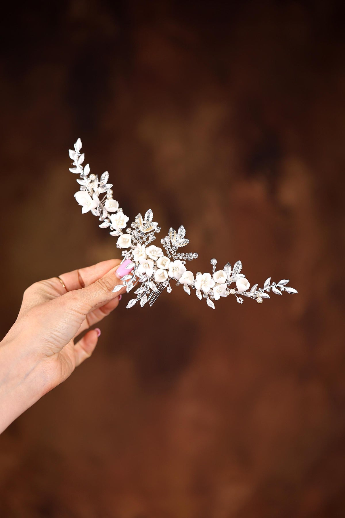a hand holding a white flower headpiece in front of a brown background